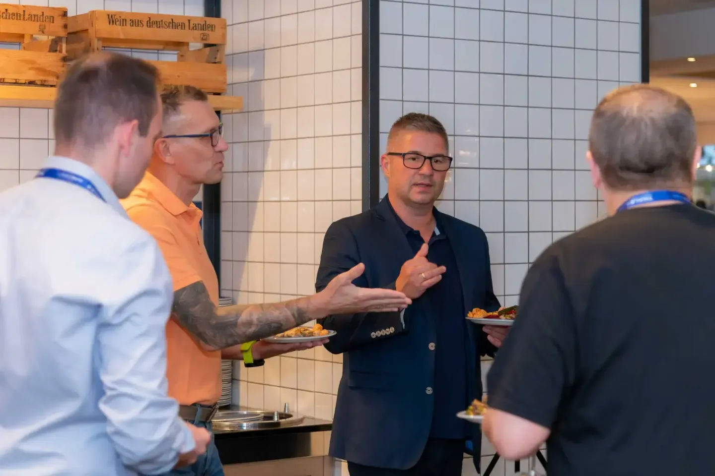 Vier Personen in Business-Kleidung unterhalten sich beim Firmenevent in Wien und halten Teller mit Speisen in der Hand