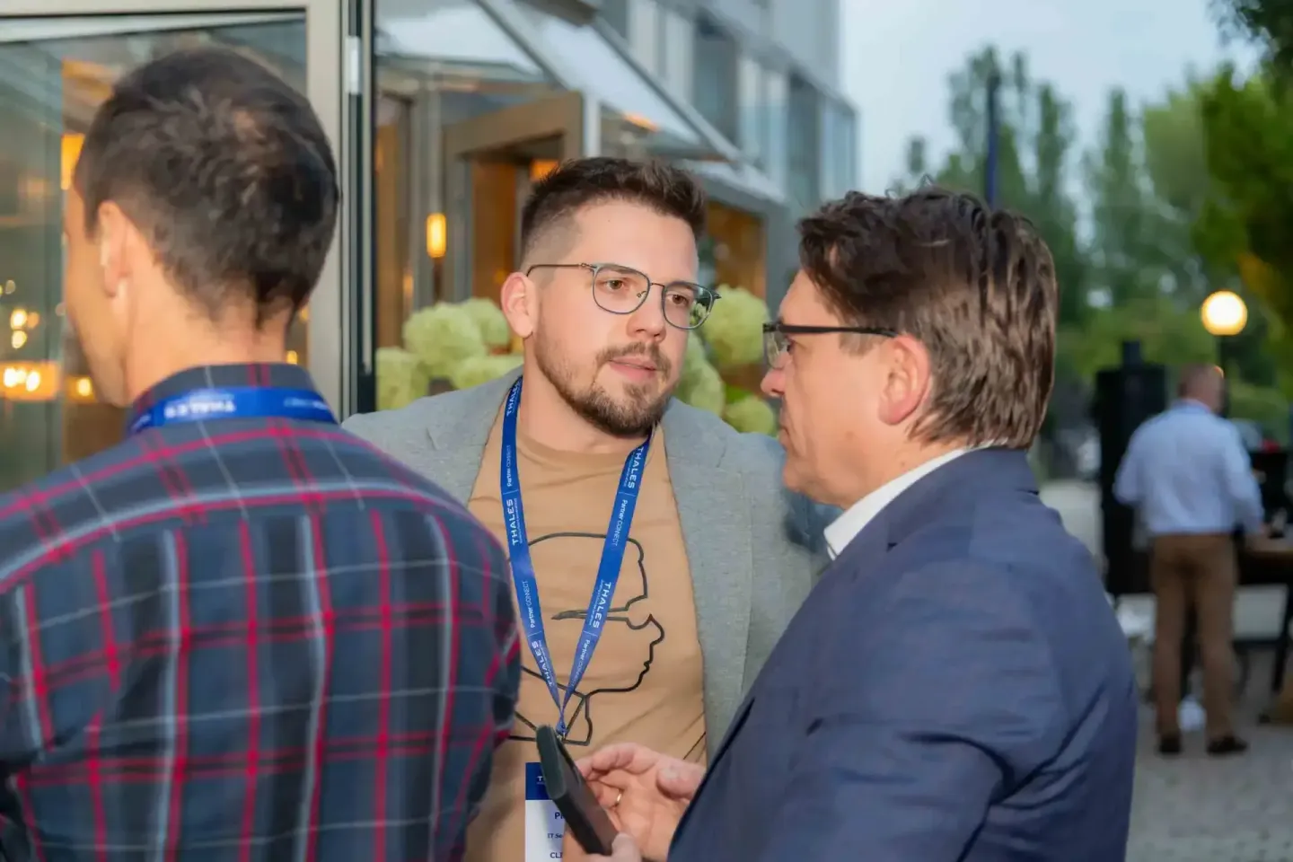 Drei Geschäftsmänner in Gespräch auf einem Firmenevent in Wien, einer trägt ein Namensschild