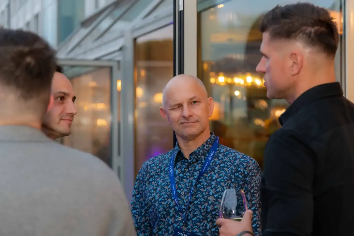Drei Männer im Gespräch bei einem Firmenevent in Wien, der mittlere trägt ein blaues Hemd und Namensschild