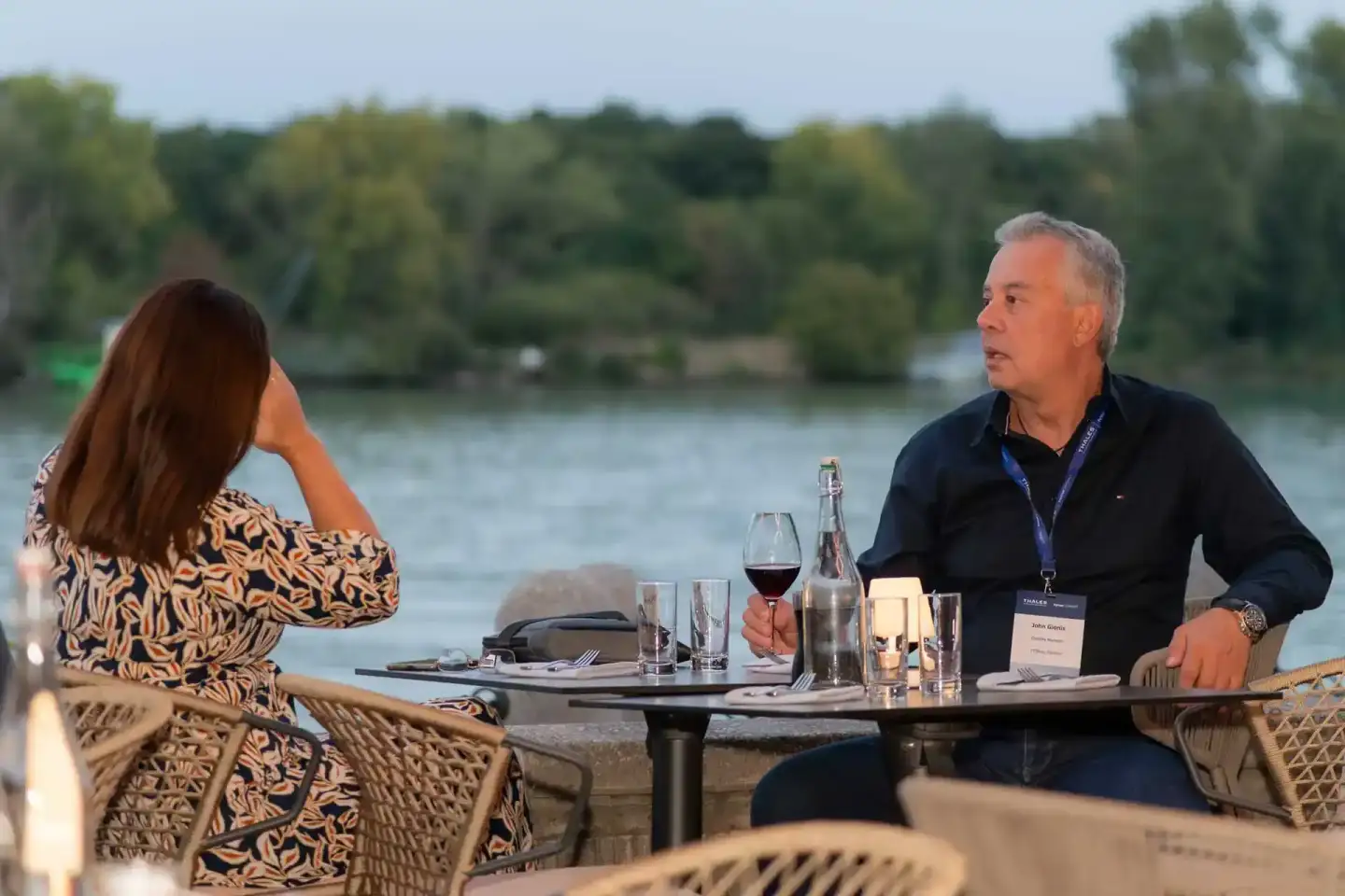 Eventfotograf dokumentiert Geschäftsmeeting zweier Personen an Tisch mit Blick auf Fluss und Grünflächen