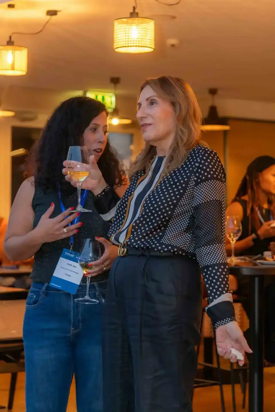 Zwei Frauen beim Networking auf einem Firmenevent in Wien, eine hält ein Weinglas und trägt ein Namensschild