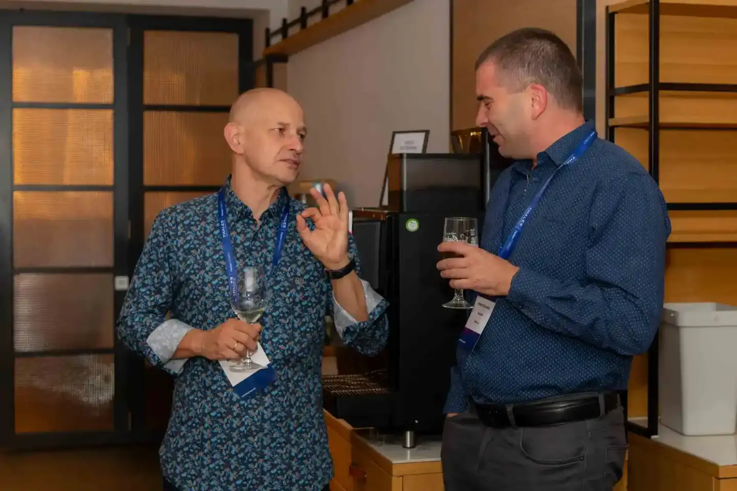Zwei Geschäftsmänner im Gespräch auf einem Firmenevent Wien, beide tragen blaue Hemden und Badges