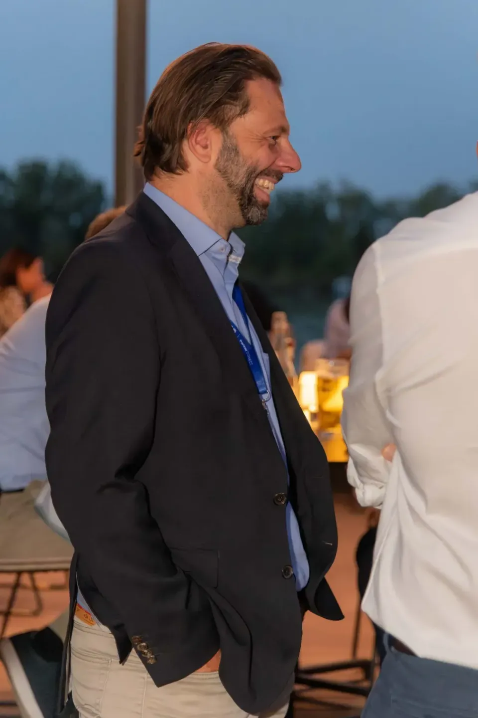 Geschäftsmann lächelnd bei Firmenevent Wien, trägt dunkles Sakko und blaues Hemd mit Namensschild