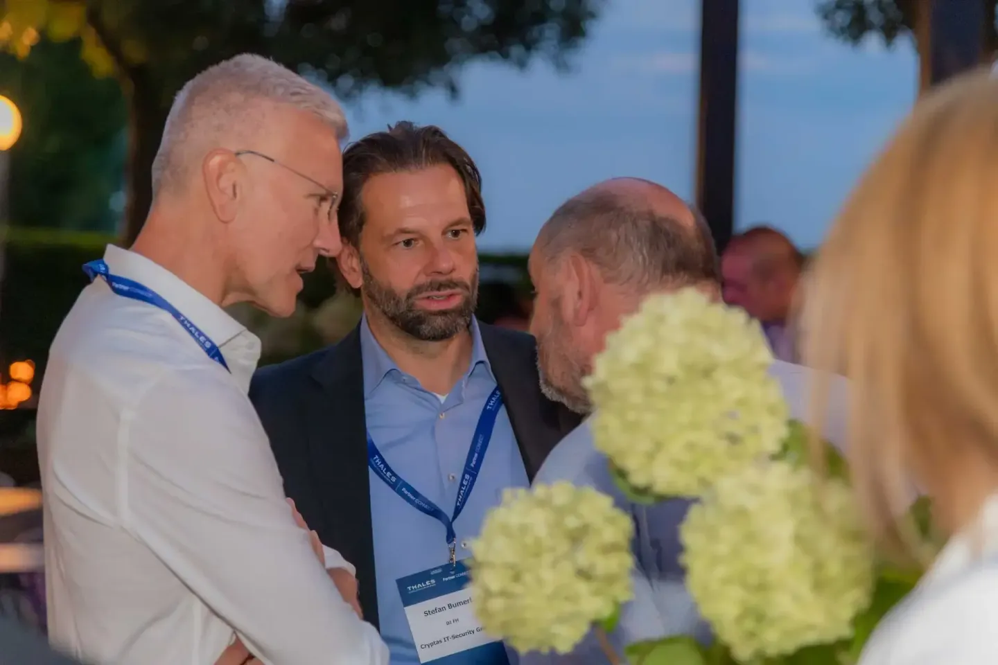 Drei Geschäftsmänner im Gespräch bei einem Firmenevent Wien, einer trägt ein Namensschild, im Vordergrund Blumendekoration