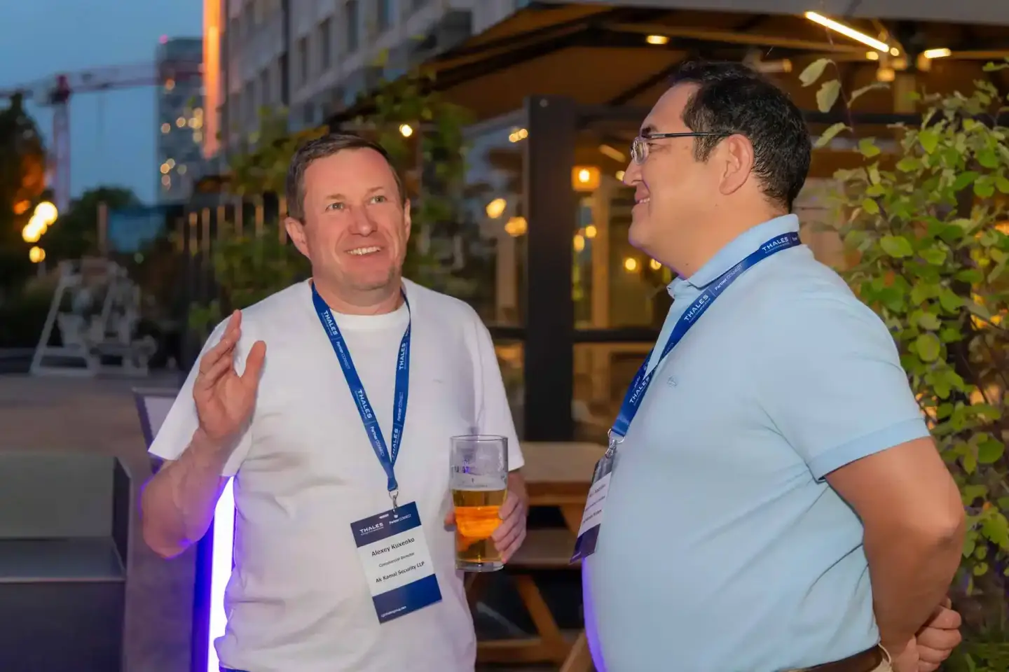 Zwei Männer mit Namensschildern unterhalten sich beim Thales Firmenevent in Wien, einer hält ein Glas mit Getränk