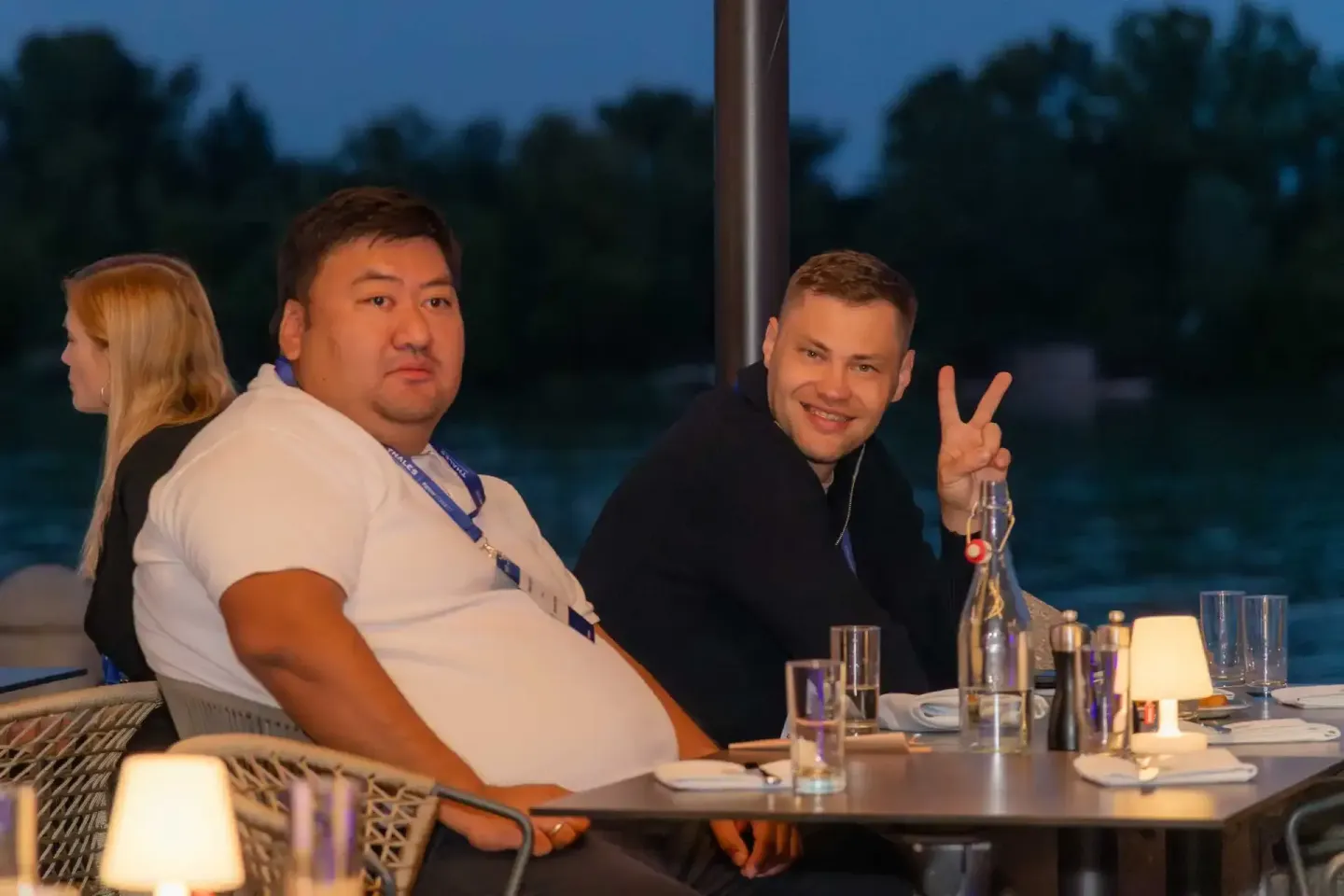 Zwei Männer und eine Frau bei einem Firmenevent Wien an einem Tisch mit Getränken, einer macht ein Victory-Zeichen