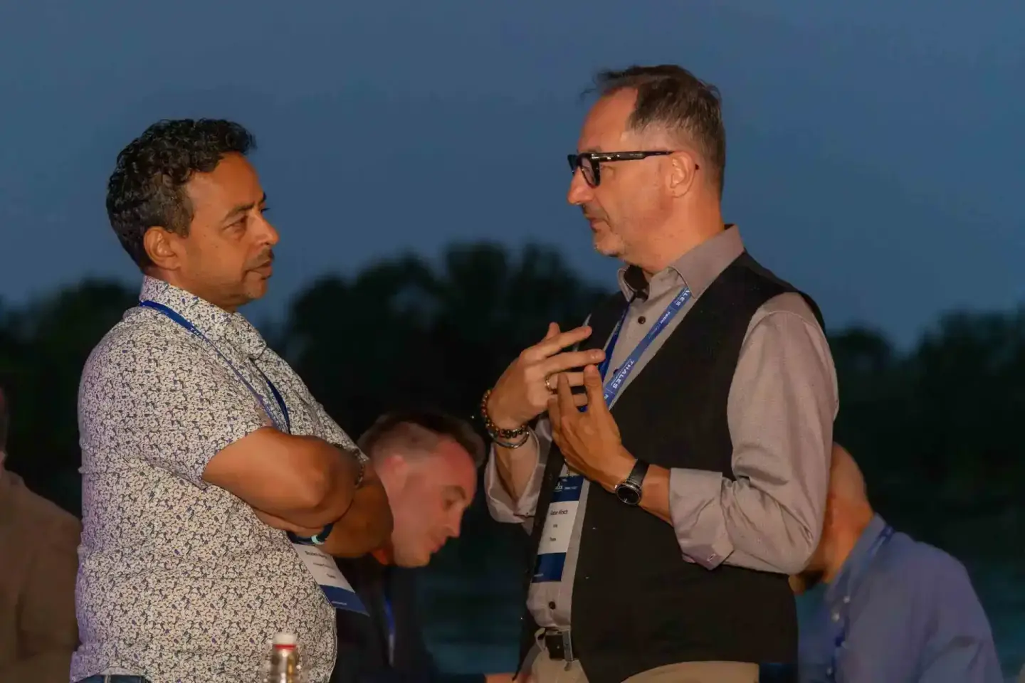 Zwei Männer im Gespräch bei einem Firmenevent Wien, einer trägt ein gemustertes Hemd, der andere Brille und ein Namensschild