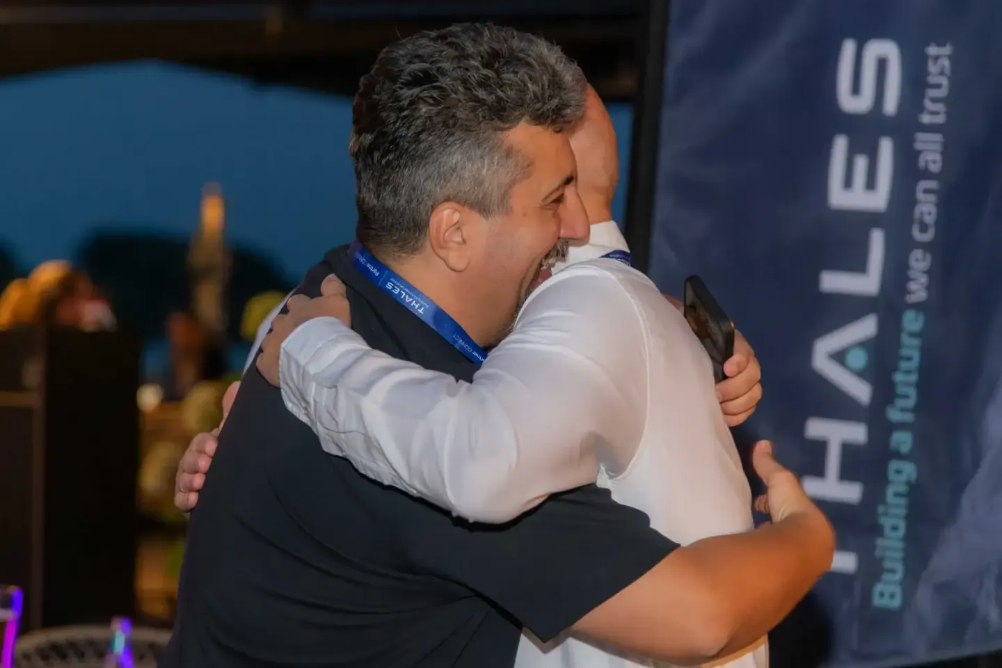 Zwei Männer umarmen sich herzlich bei einem Firmenevent Wien, einer trägt ein Lanyardband