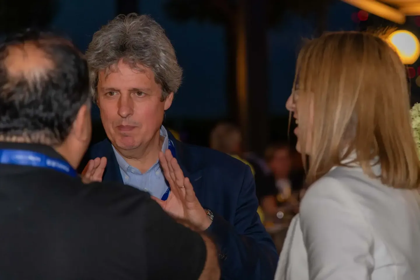 Geschäftsmann in dunklem Blazer im Gespräch mit zwei Personen auf einem Firmenevent Wien