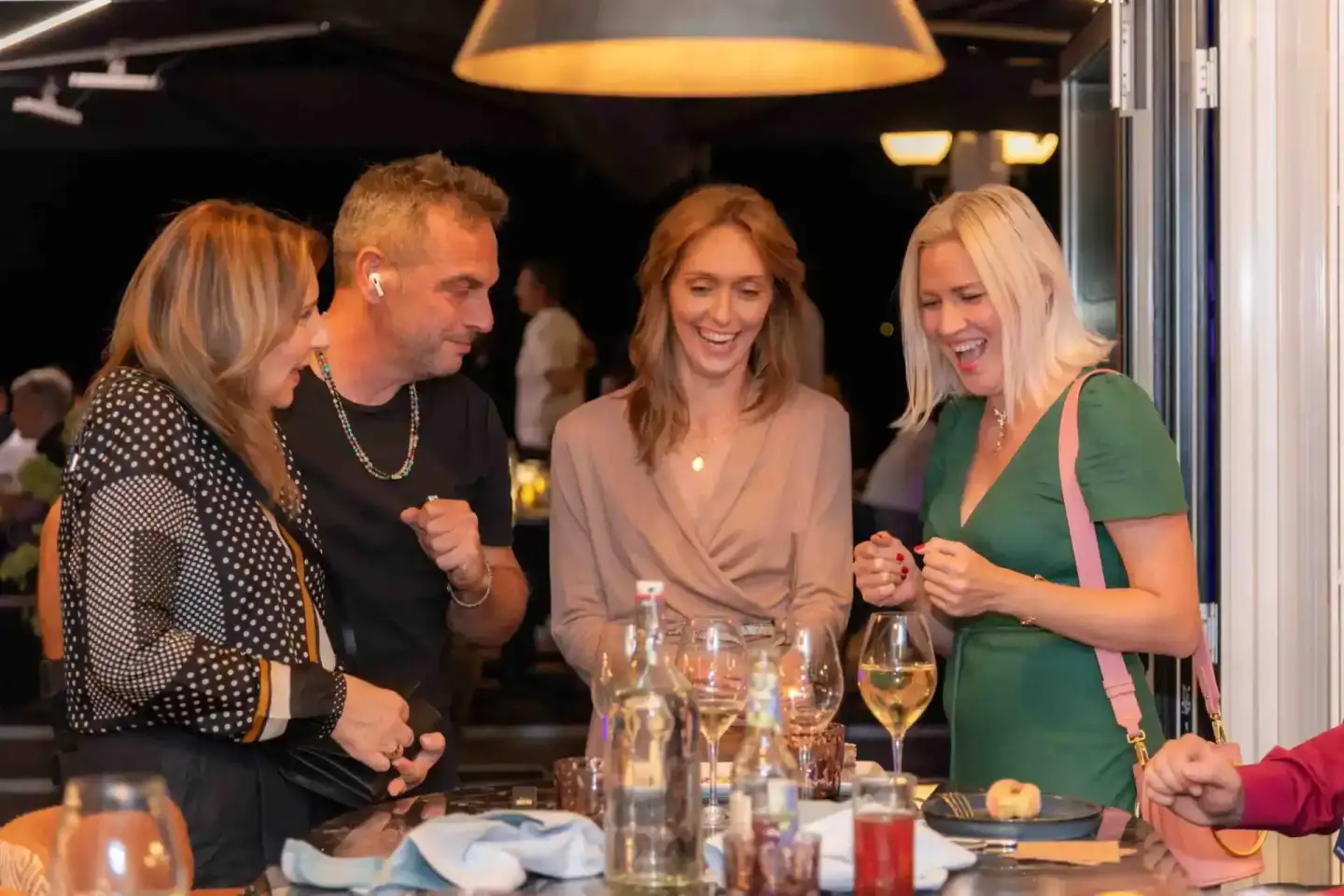 Vier lachende Gäste an einem Tisch bei einem Firmenevent Wien, mit Weingläsern und festlicher Atmosphäre