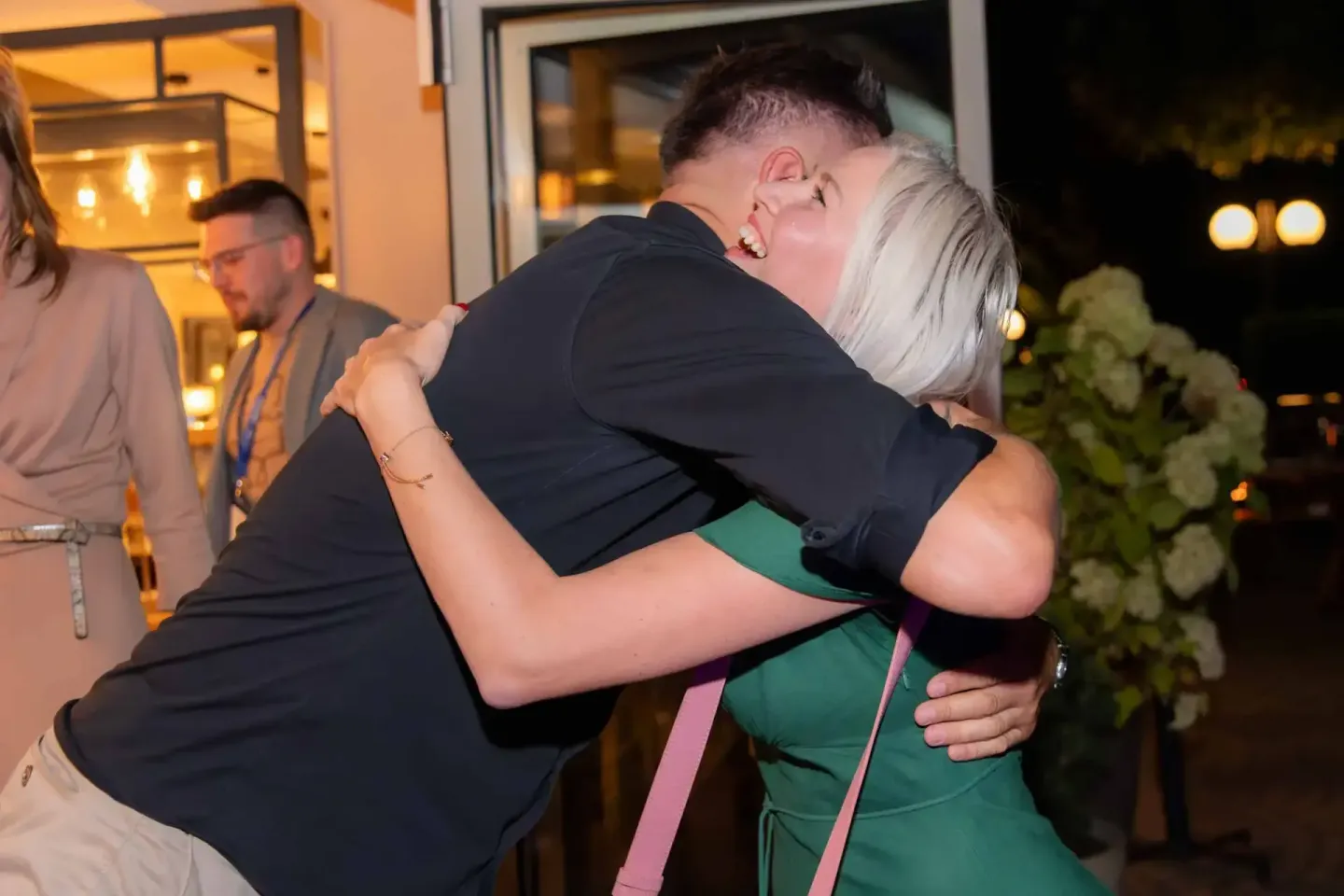 Zwei Personen umarmen sich herzlich bei einem Firmenevent in Wien, im Hintergrund andere Gäste und beleuchtete Eingangsbereic