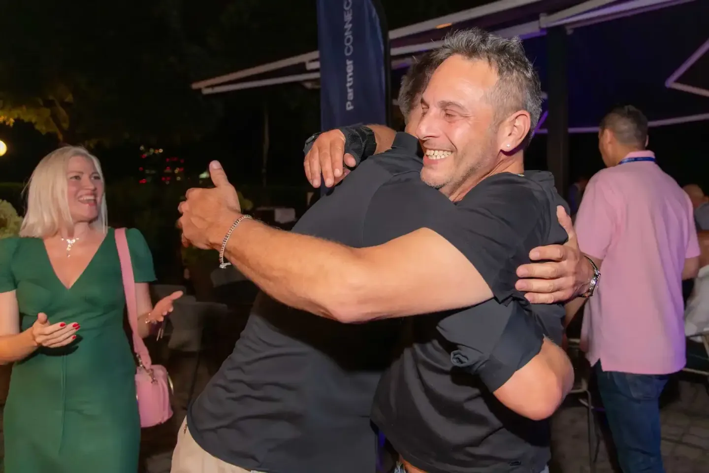 Zwei Männer umarmen sich herzlich auf einem Firmenevent in Wien, im Hintergrund Gäste und Veranstaltungszelt