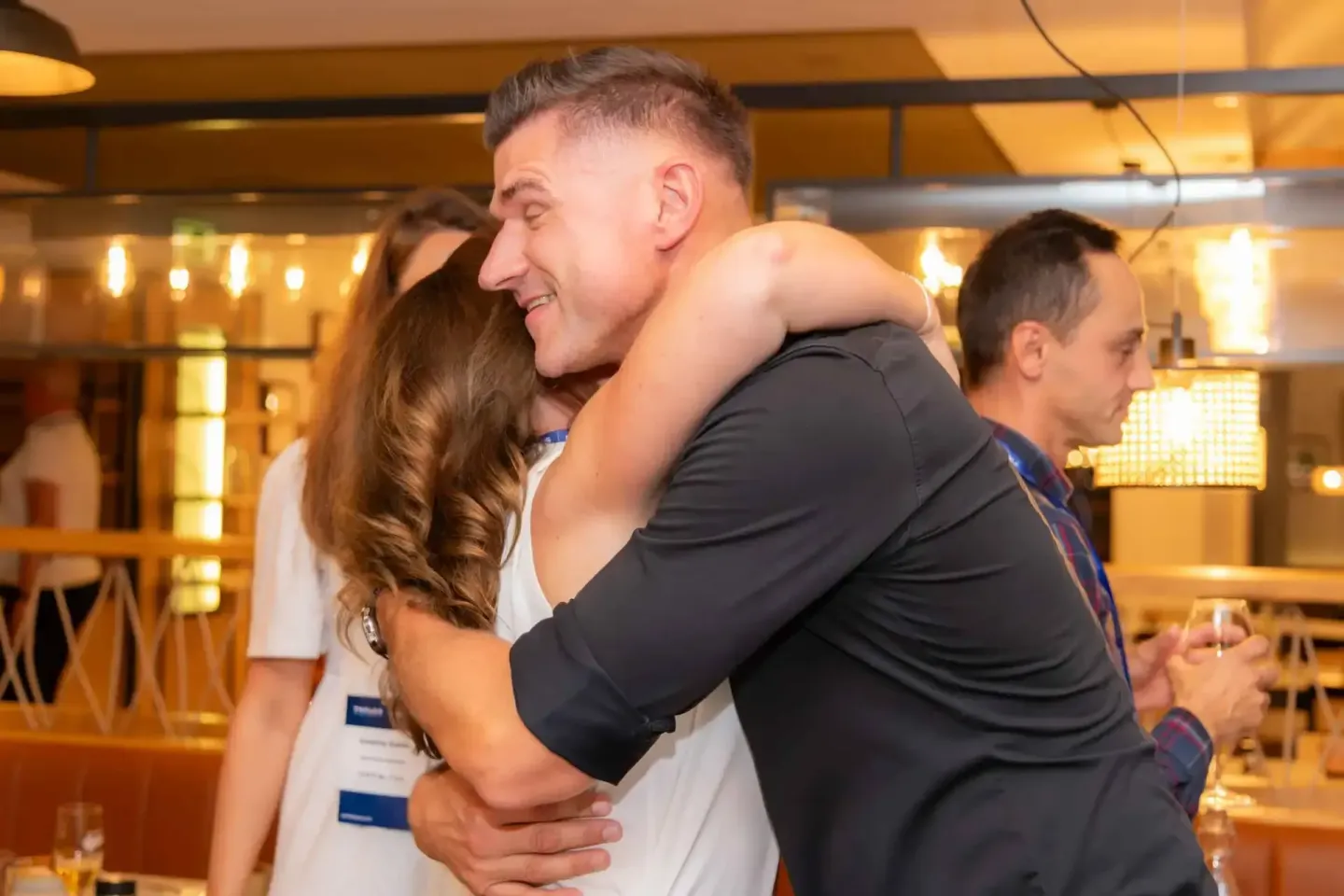 Mann trägt lachende Frau auf seinen Schultern bei einem Firmenevent in Wien, festliche Atmosphäre im Hintergrund