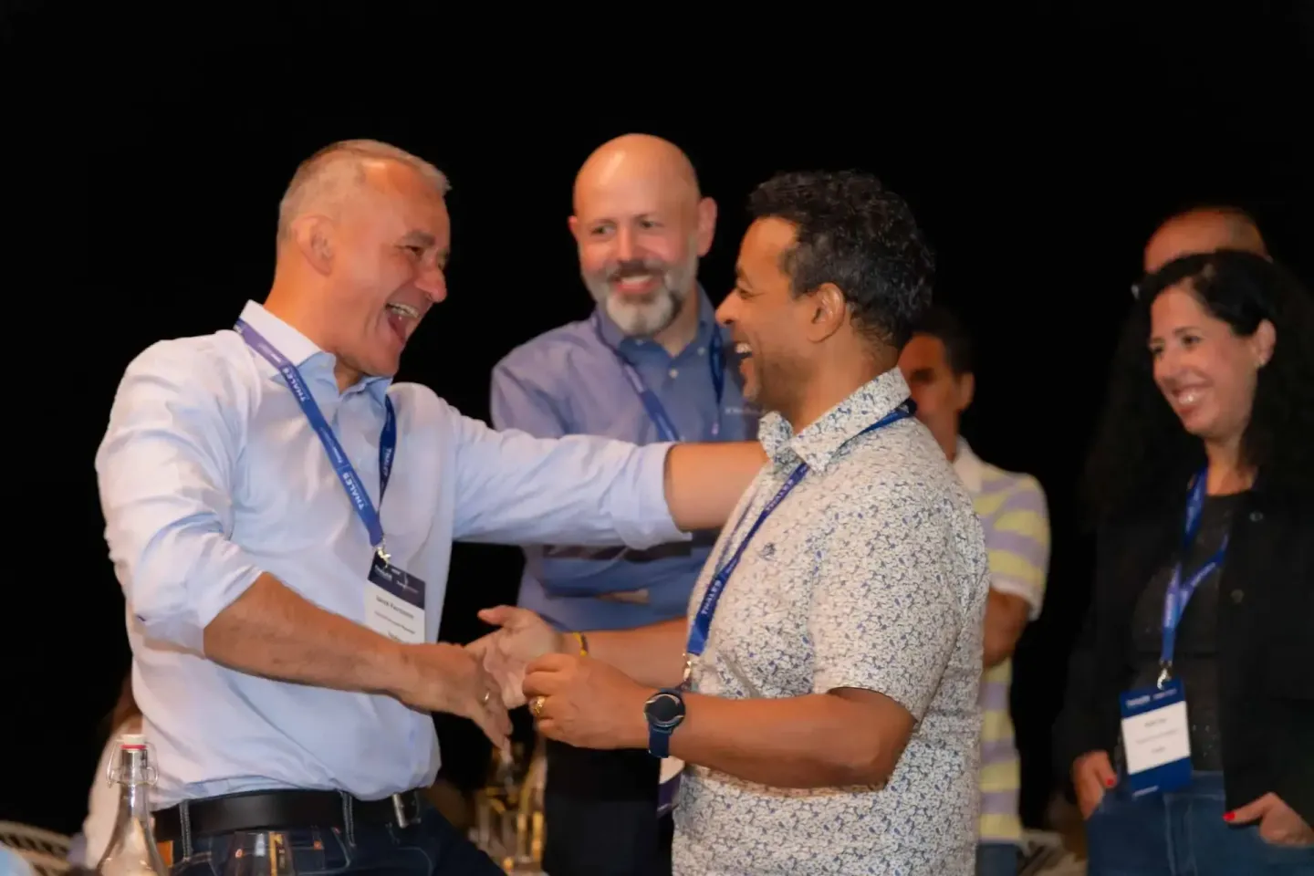 Eventfotograf Wien dokumentiert freundliche Begegnung zwischen zwei Männern auf Firmenevent, weitere Gäste im Hintergrund