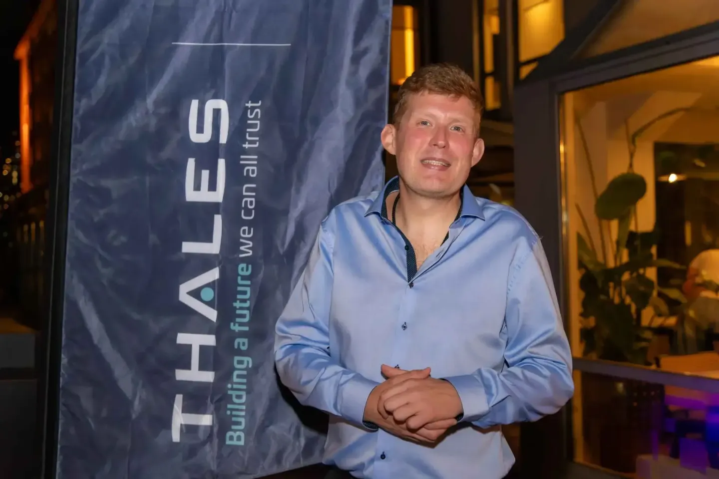 Mann in hellblauem Hemd spricht vor Thales Banner auf Firmenevent Wien