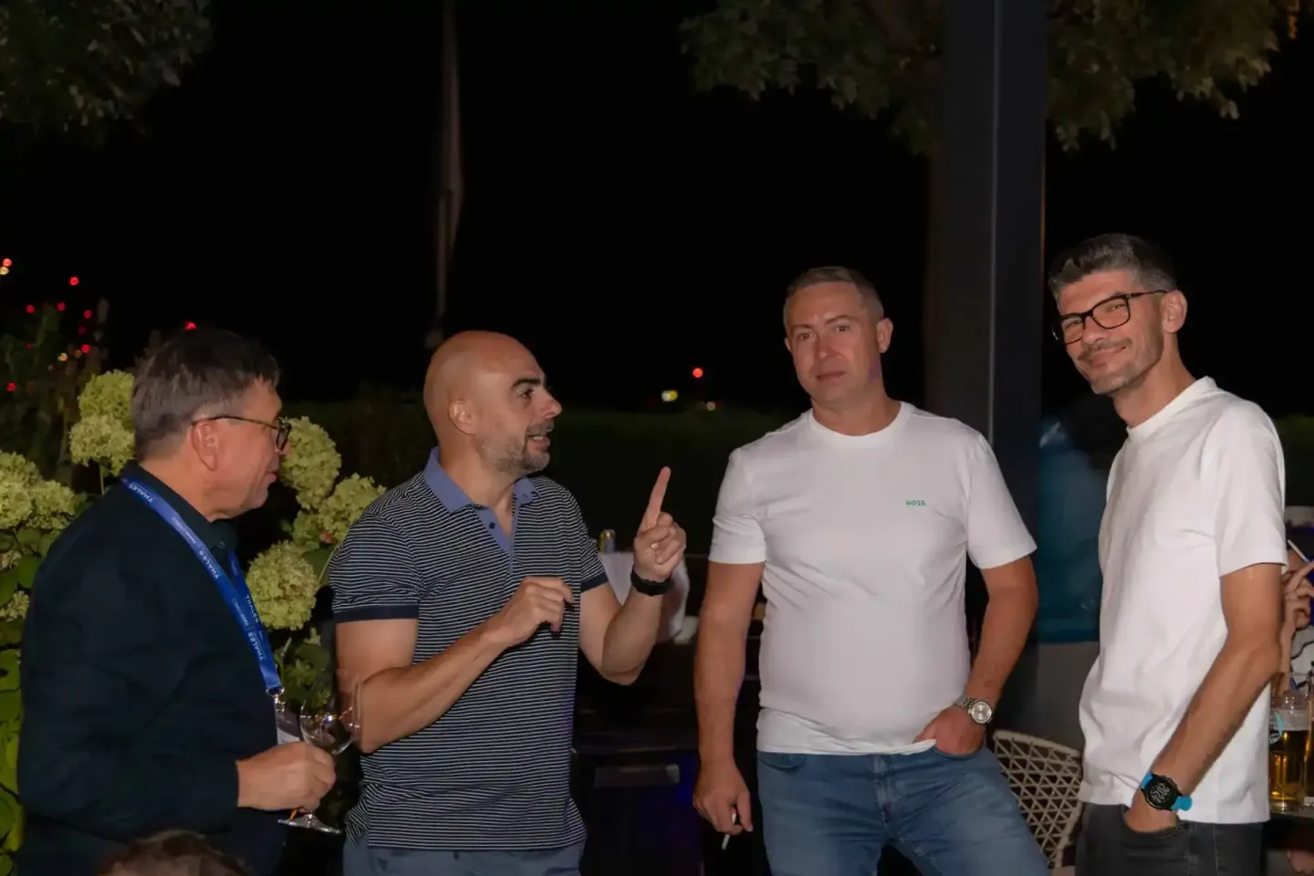 Vier Männer im Gespräch bei einem Firmenevent Wien am Abend, mit Getränken und beleuchteter Gartenanlage im Hintergrund