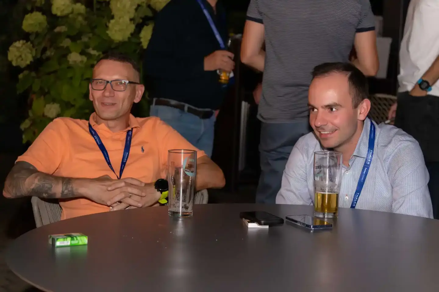 Zwei Männer mit Lanyards sitzen an einem Tisch beim Thales Firmenevent in Wien und unterhalten sich entspannt