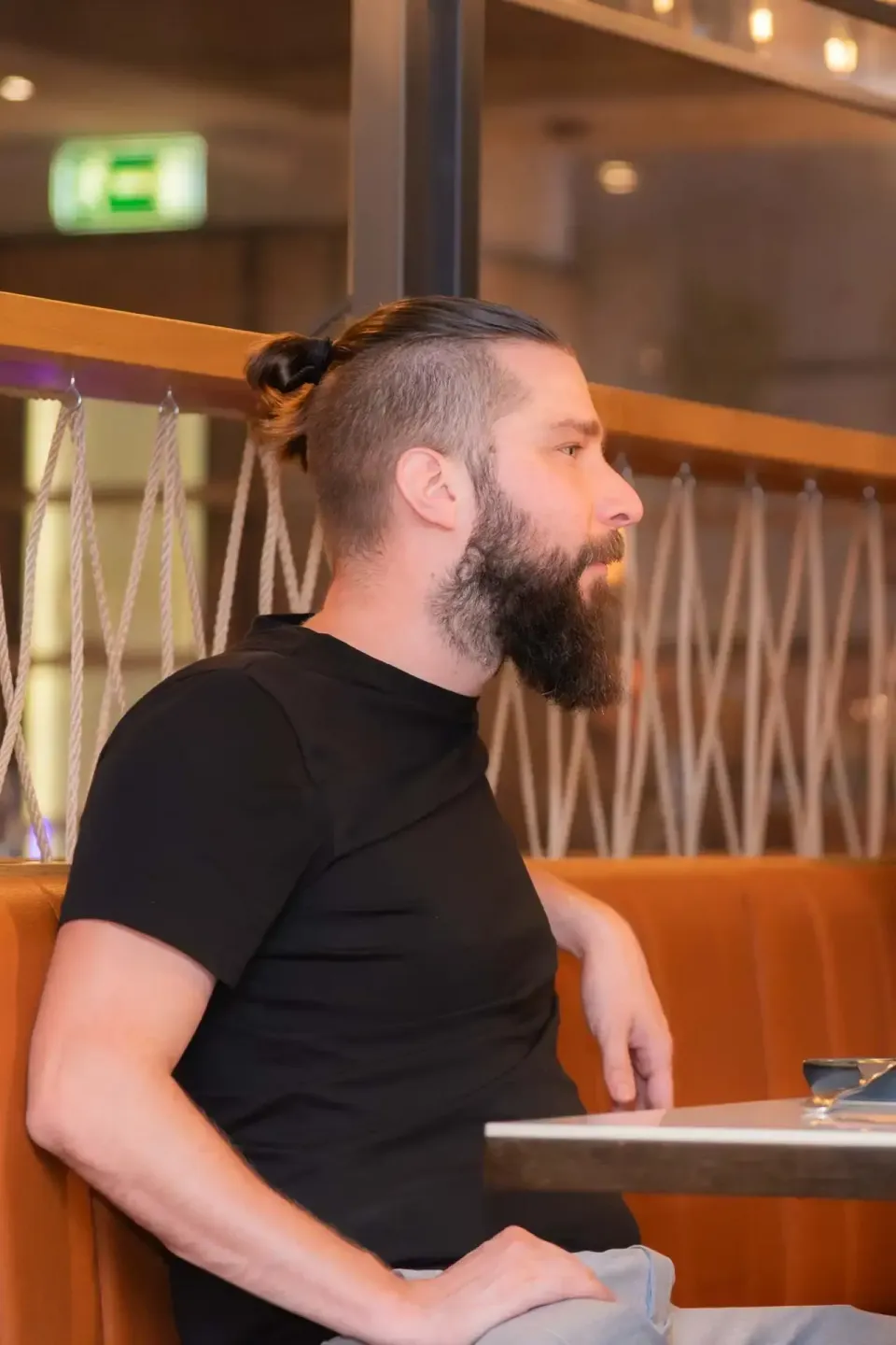 Mann mit Bart und Dutt sitzt auf orangefarbener Bank bei Firmenevent Wien, im Hintergrund modernes Interieur