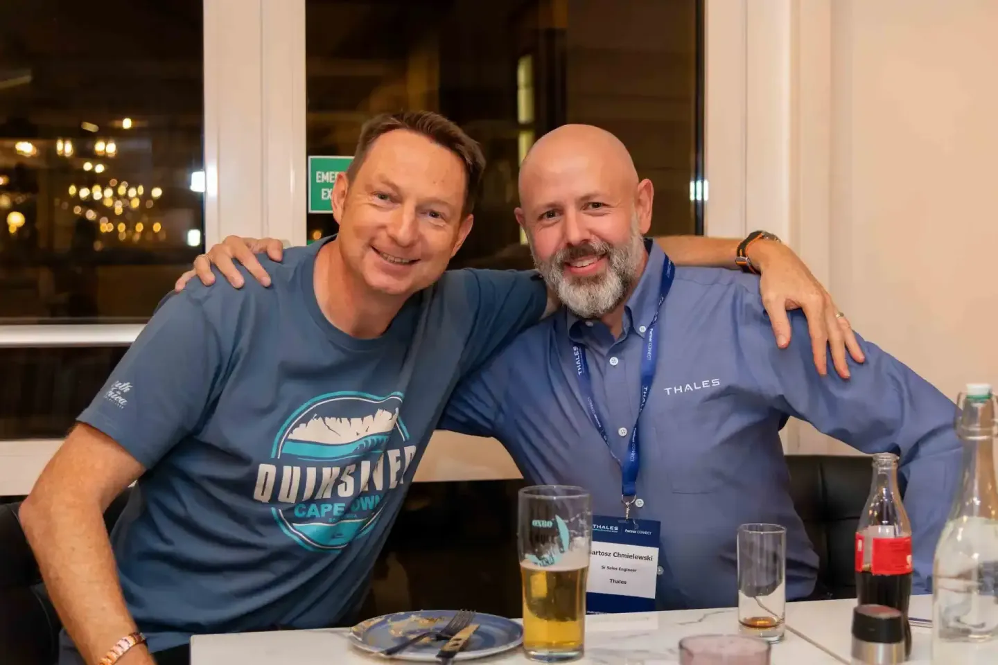 Zwei Männer posieren lächelnd bei einem Firmenevent Wien, einer trägt ein blaues Thales-Poloshirt