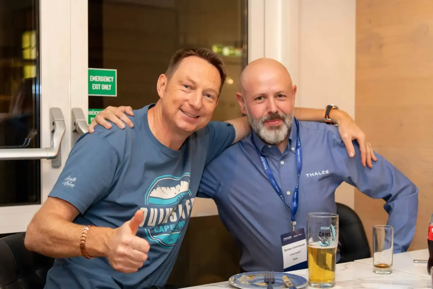 Zwei Männer bei einem Firmenevent Wien, einer trägt ein blaues Shirt mit Logo, der andere ein Thales-Polo-Shirt mit Namenssch