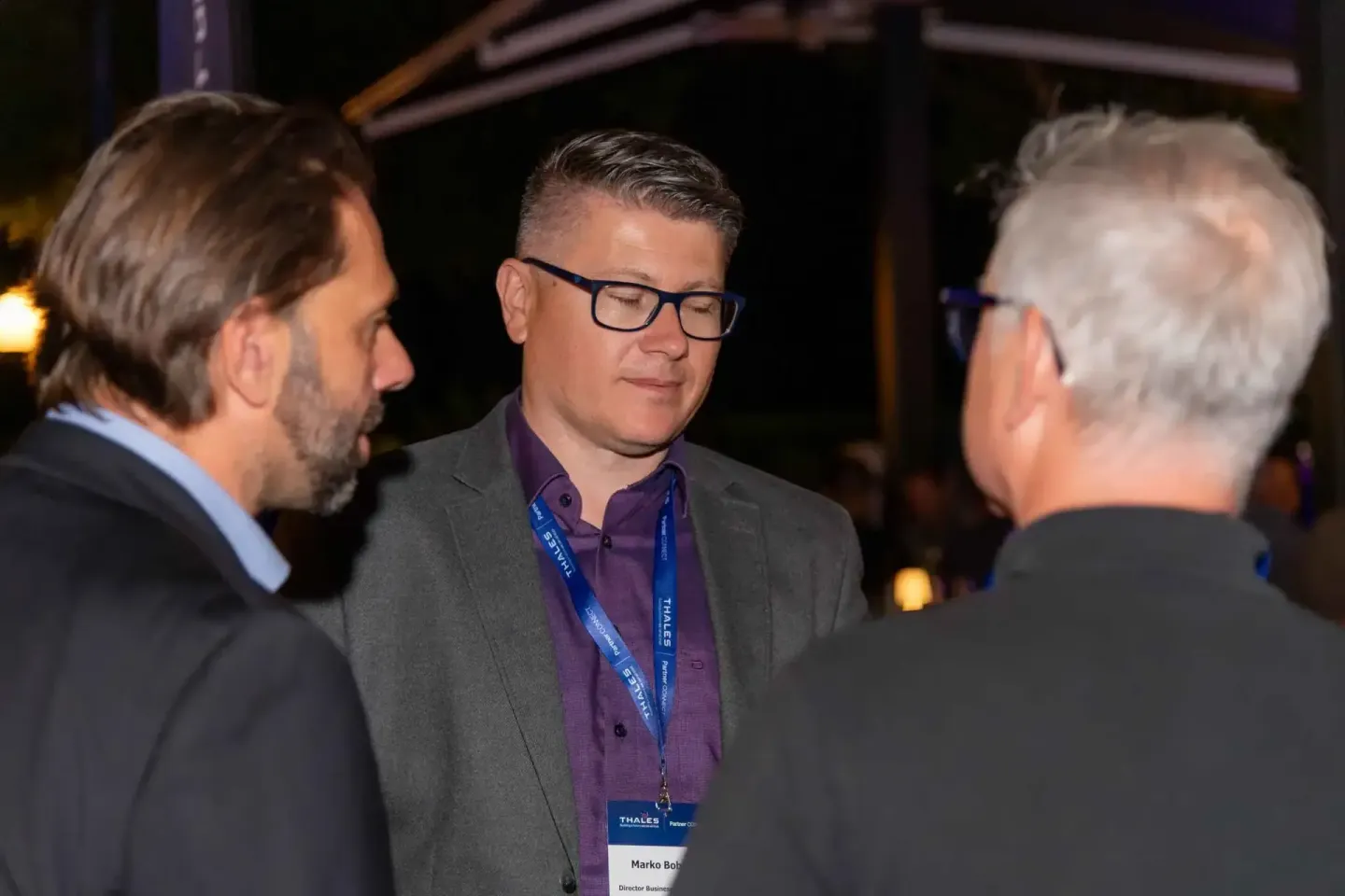 Drei Geschäftsmänner im Gespräch auf einem Firmenevent Wien mit Thales-Namensschildern und Lanyards