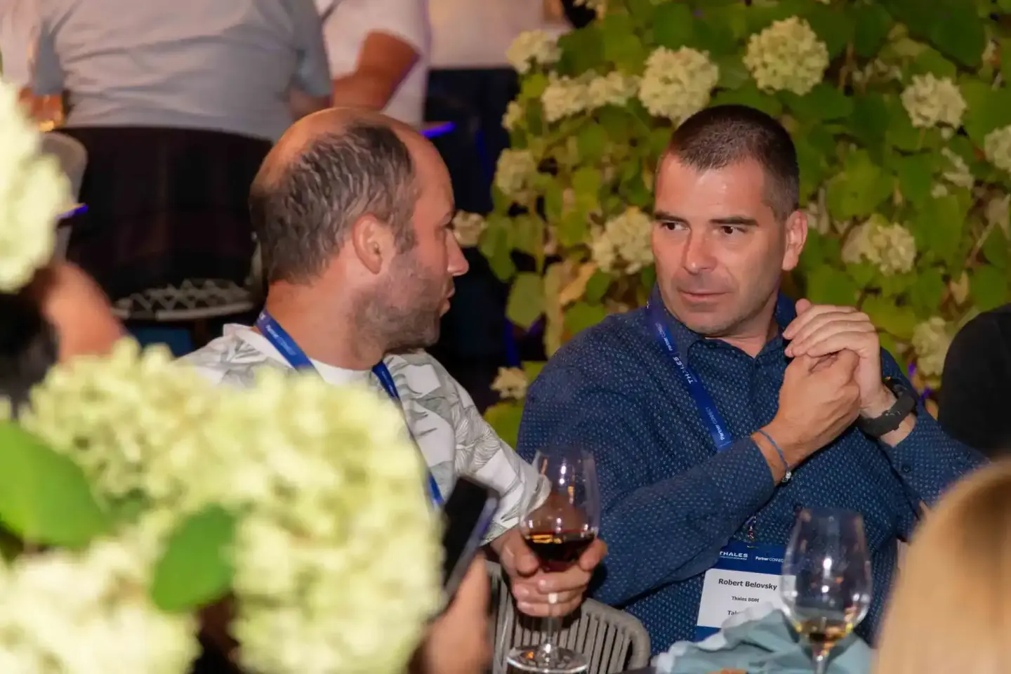 Zwei Männer im Gespräch bei einem Firmenevent Wien, einer trägt ein Namensschild, beide halten Getränke, im Hintergrund grüne