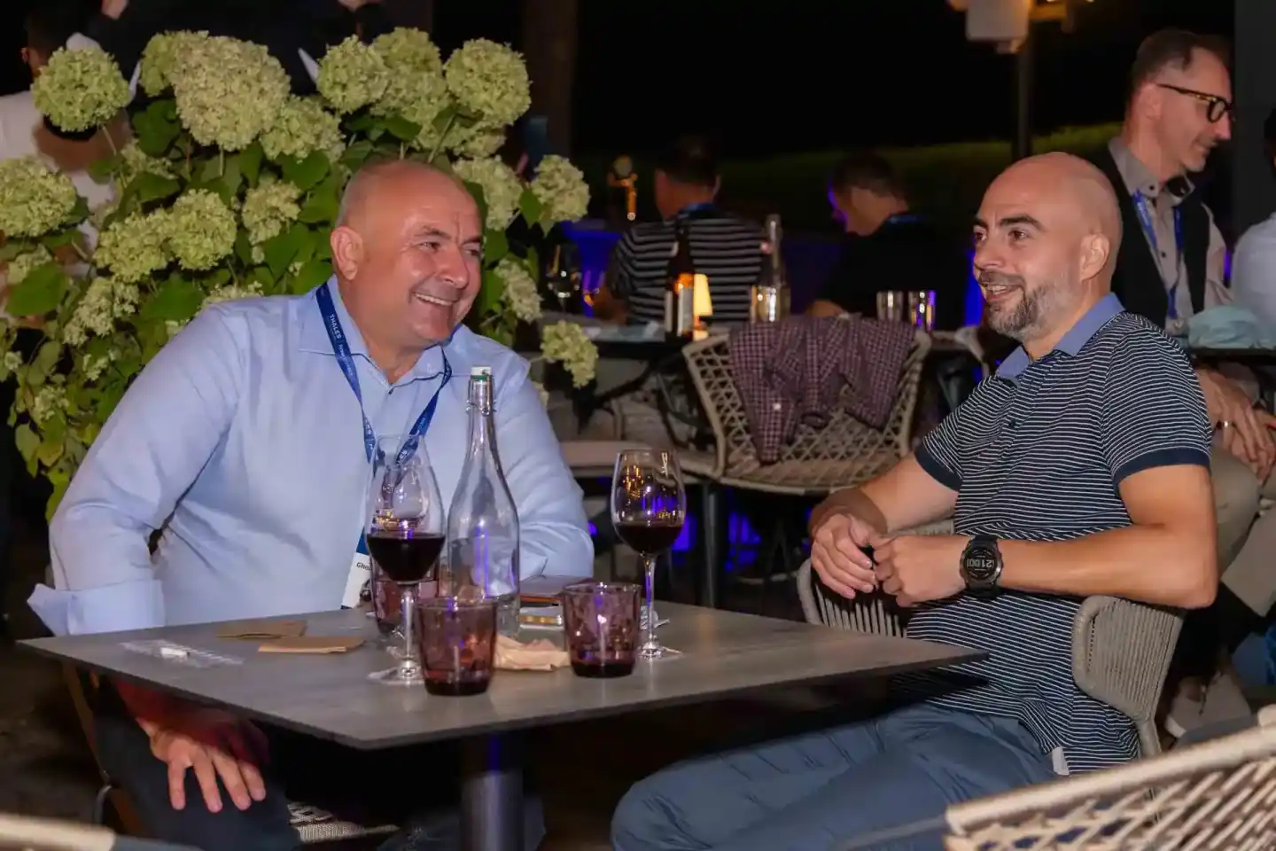 Zwei Männer beim Networking an einem Tisch mit Getränken, im Hintergrund elegante Veranstaltungsdekoration mit weißen Hortens