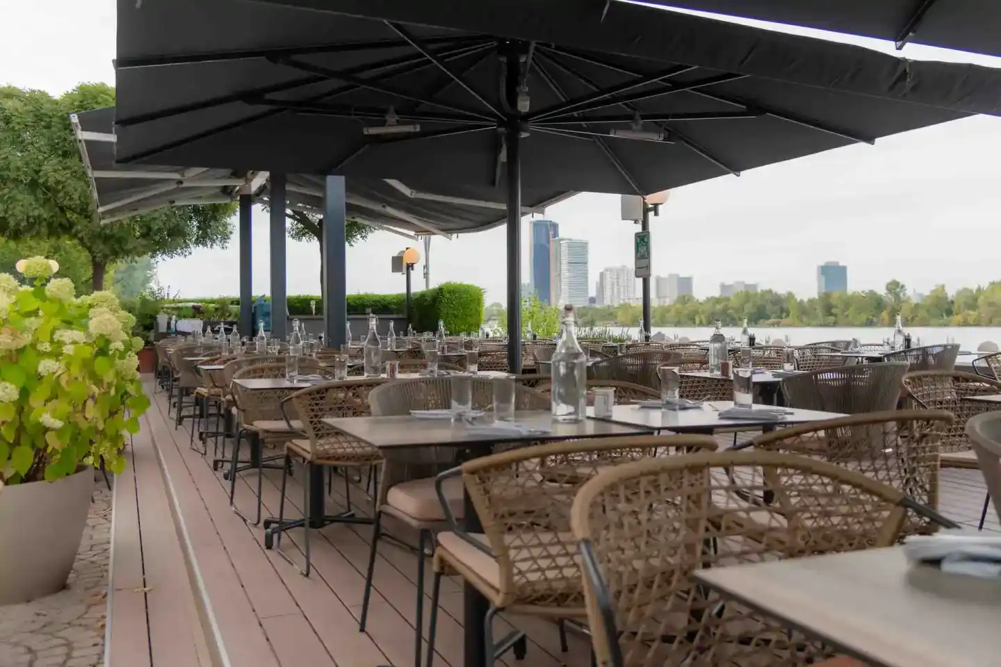 Elegante Außenterrasse mit Bestuhlung unter schwarzen Sonnenschirmen, Blick auf die Donau und Skyline - Eventfotografie Wien