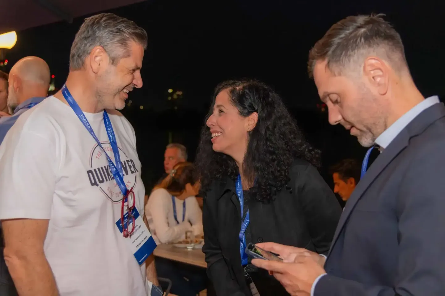 Drei Personen mit Lanyards unterhalten sich lachend bei einem Firmenevent Wien in entspannter Abendatmosphäre