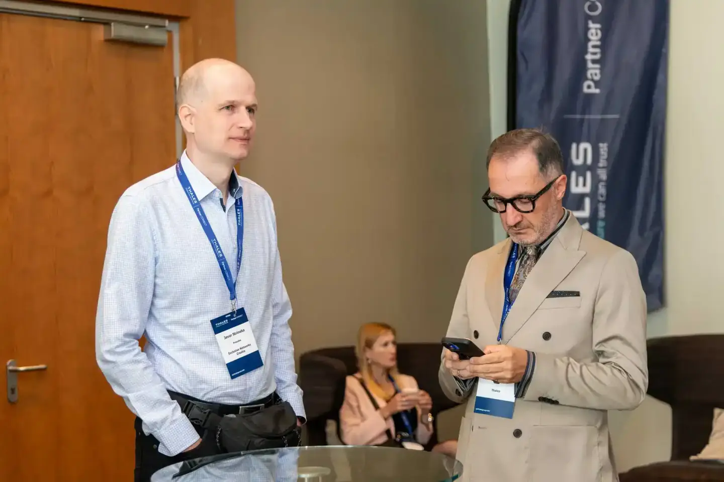 Zwei Geschäftsmänner mit Lanyards bei einem Firmenevent in Wien, einer hält ein Smartphone in der Hand