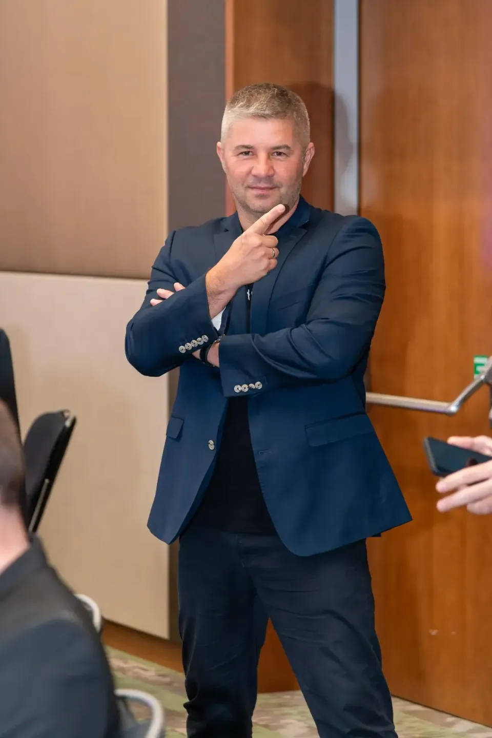Geschäftsmann in dunklem Anzug beim Thales Firmenevent Wien, selbstbewusste Pose mit überkreuzten Armen