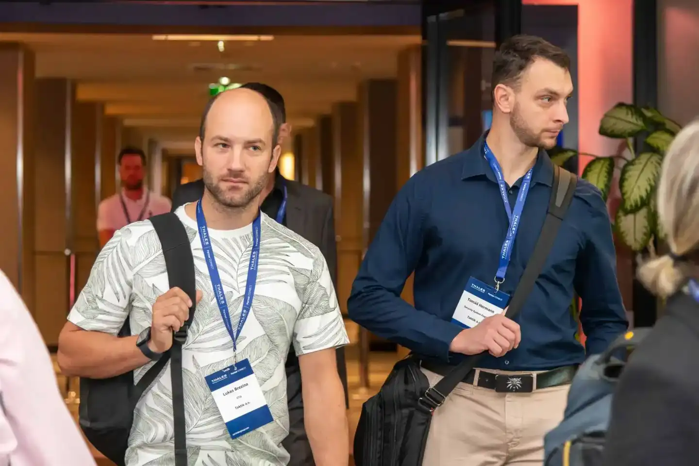 Zwei Teilnehmer mit Badges beim Thales Firmenevent Wien in einem modernen Konferenzflur, einer trägt ein beiges Hemd mit Blat