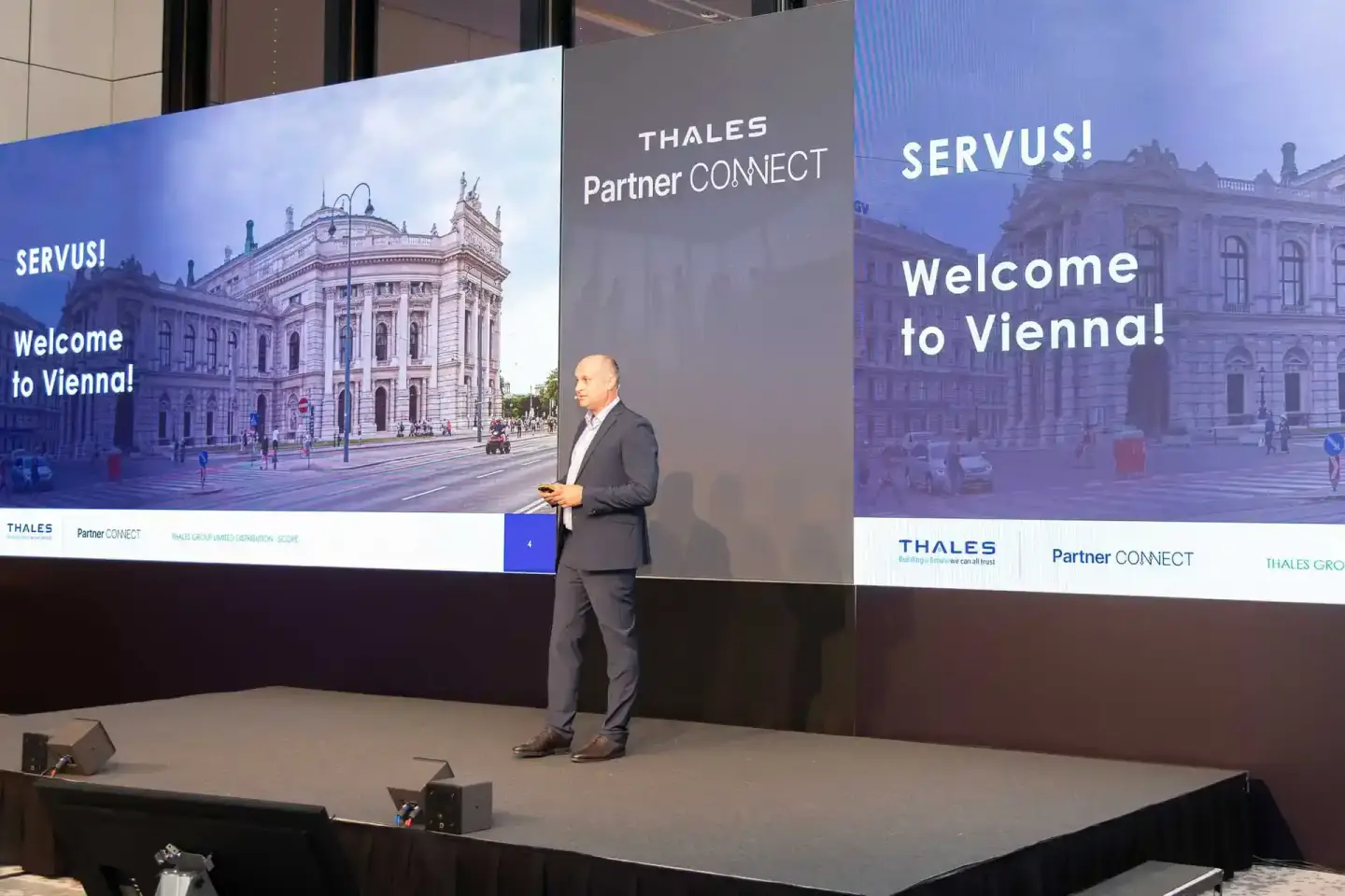 Geschäftsmann präsentiert auf der Bühne bei Thales Partner Connect Event in Wien vor großer Videowand mit Wiener Sehenswürdig
