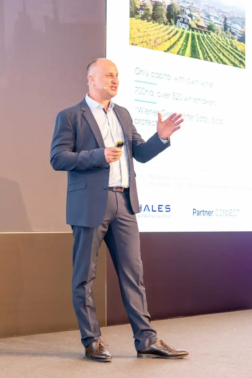 Geschäftsmann präsentiert beim Thales Firmenevent Wien vor Publikum mit Weinberg-Hintergrund auf Präsentationsfläche