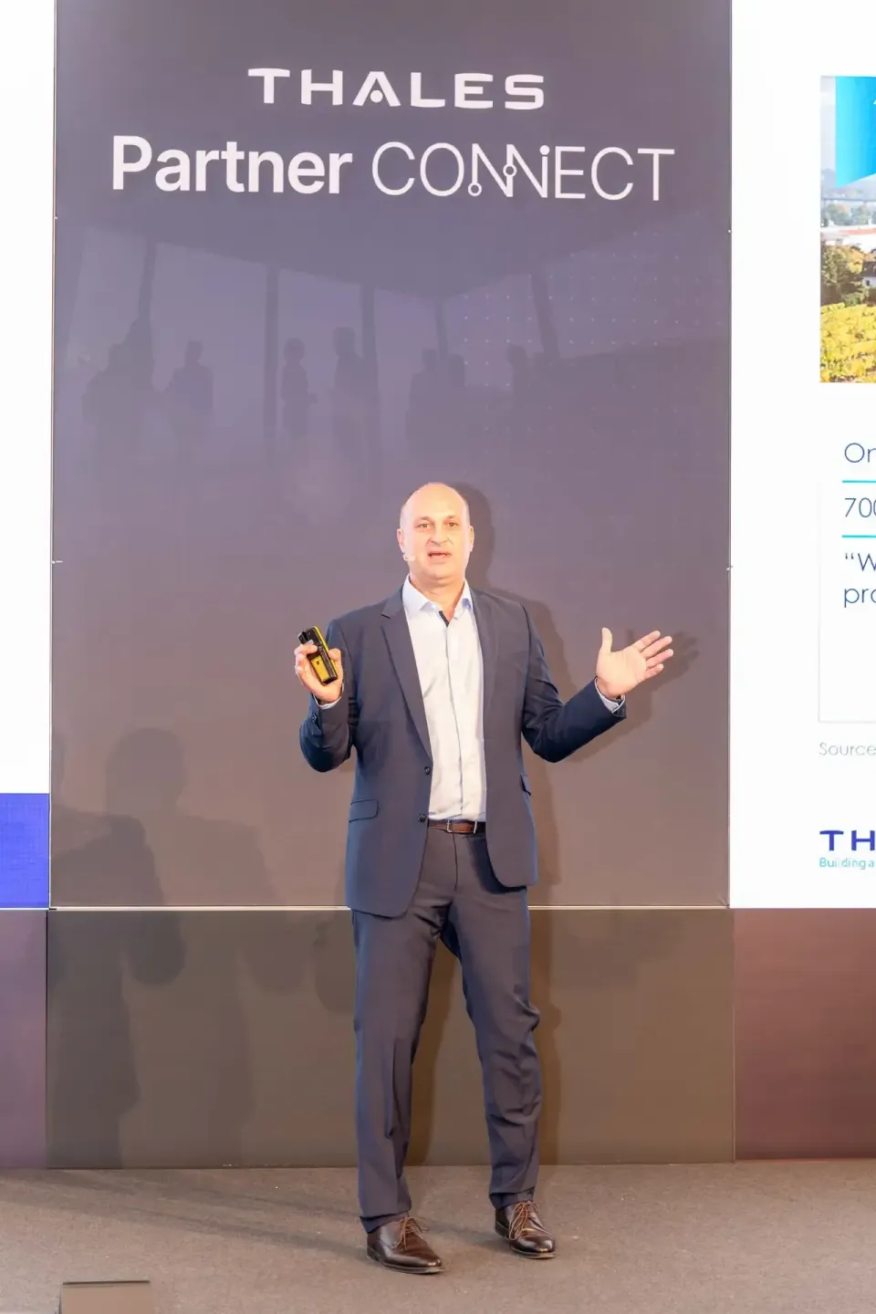 Geschäftsmann präsentiert auf Thales Partner Connect Veranstaltung ein gelbes Gerät vor Publikum - Eventfotografie Wien