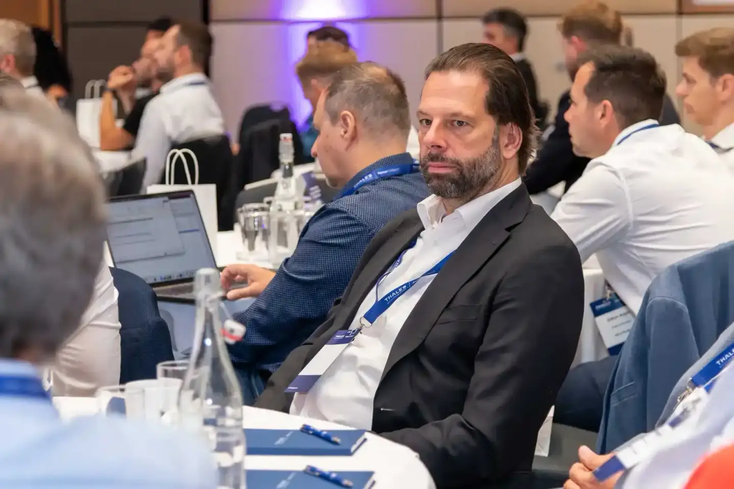 Geschäftsmann mit Laptop bei Thales Firmenevent Wien, im Hintergrund weitere Teilnehmer an Konferenztischen