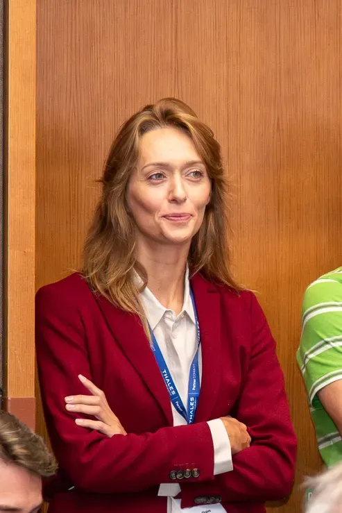 Profesionelle Frau in rotem Blazer bei Firmenevent Wien, trägt Konferenz-Badge und lächelt in die Kamera