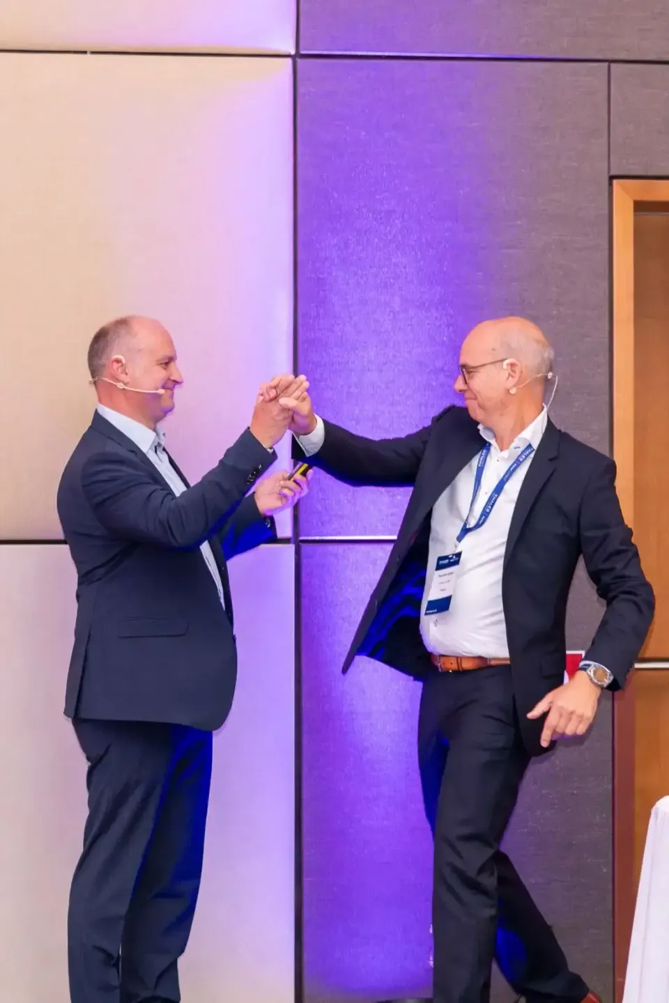 Zwei Geschäftsmänner begrüßen sich auf einem Firmenevent in Wien mit Handschlag vor lila beleuchteter Wand