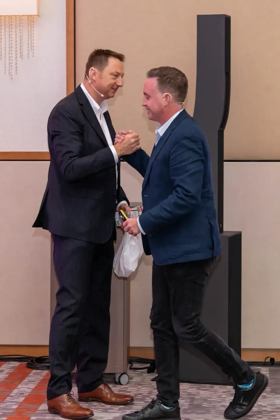 Zwei Geschäftsmänner in Anzügen schütteln sich die Hände bei einem Firmenevent in Wien, einer hält eine Medaille in der Hand