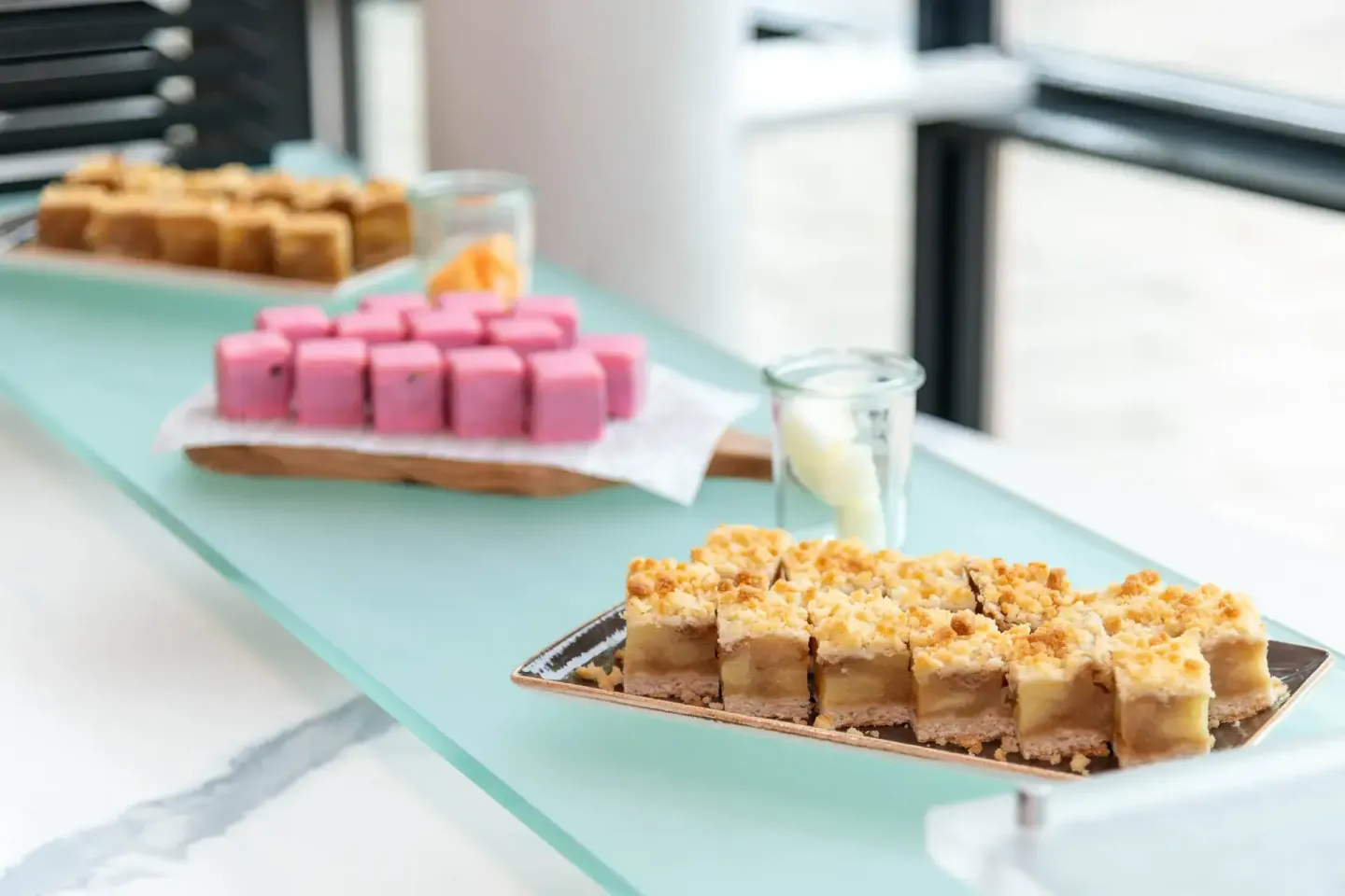 Elegante Dessert-Präsentation bei Firmenevent Wien mit rosa Petit Fours, Karamell-Schnitten und Getränk auf mintgrünem Tisch