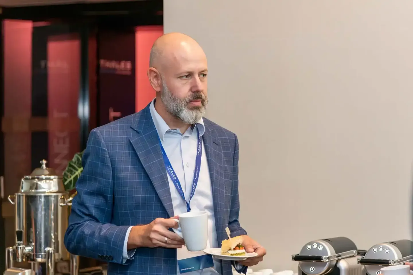 Geschäftsmann mit Bart in blauem Sakko hält Kaffee und Gebäck bei Firmenevent Wien