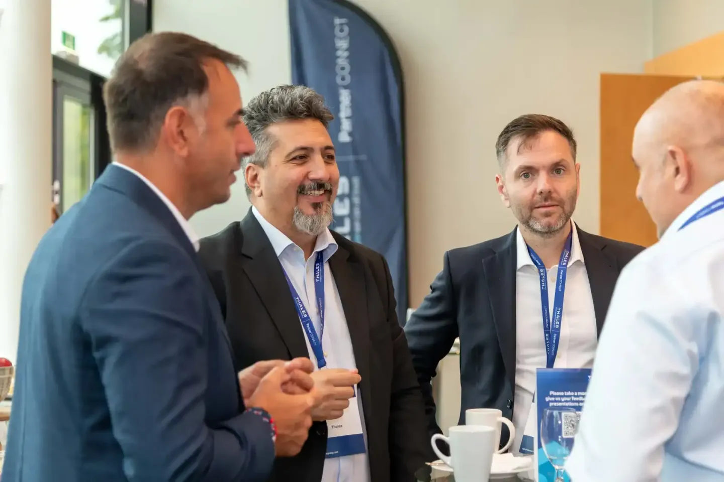 Vier Geschäftsmänner im Gespräch bei einem Firmenevent in Wien, zwei tragen Namensschilder