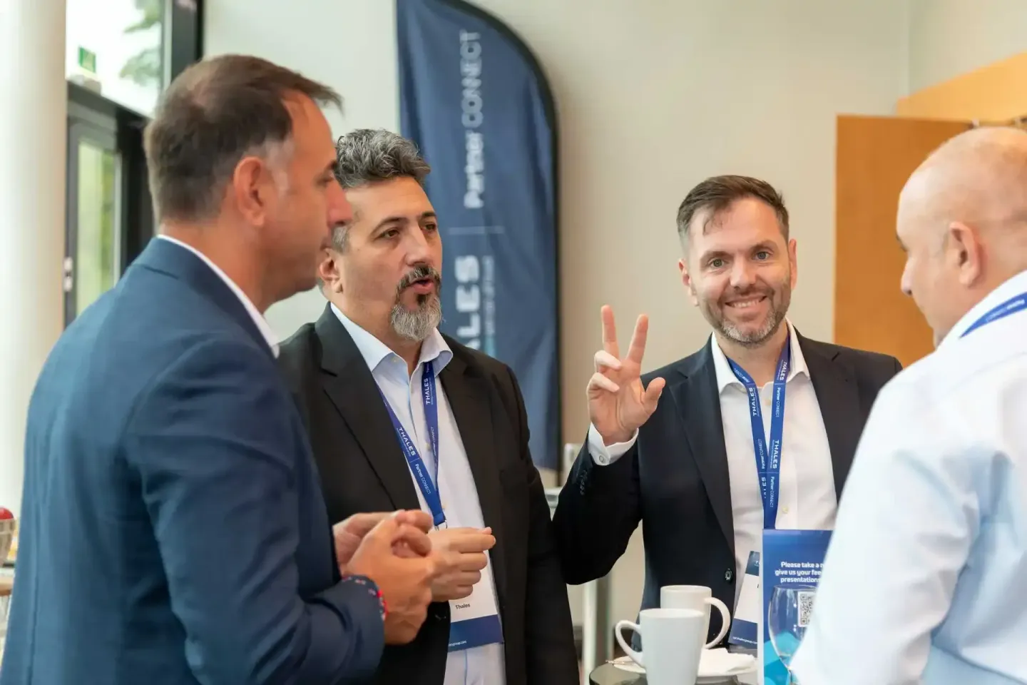 Vier Geschäftsmänner in Business-Kleidung mit Namensschildern diskutieren animiert auf einem Firmenevent Wien