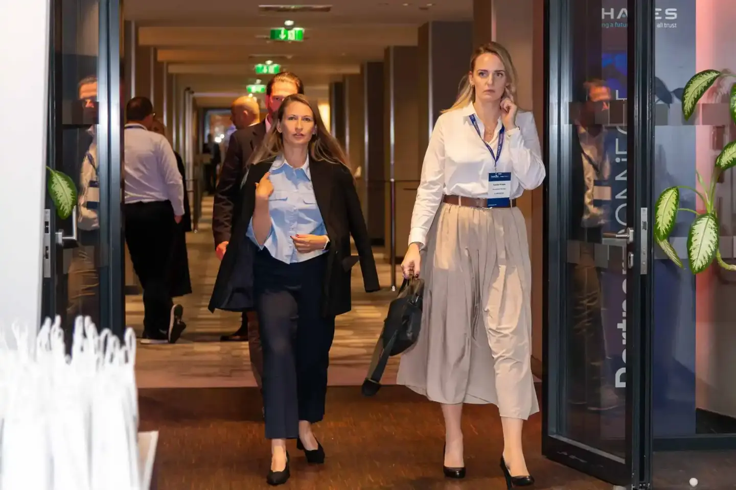 Zwei Frauen in Business-Kleidung gehen durch einen modernen Konferenzflur während eines Firmenevent Wien, im Hintergrund weit