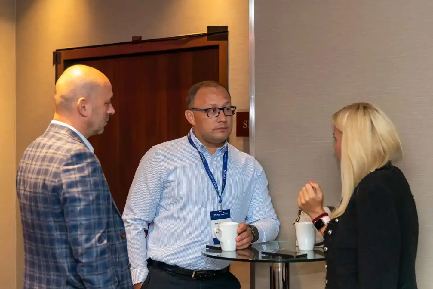 Drei Personen im geschäftlichen Gespräch bei einem Firmenevent Wien, Mann mit Brille hält Kaffeetasse