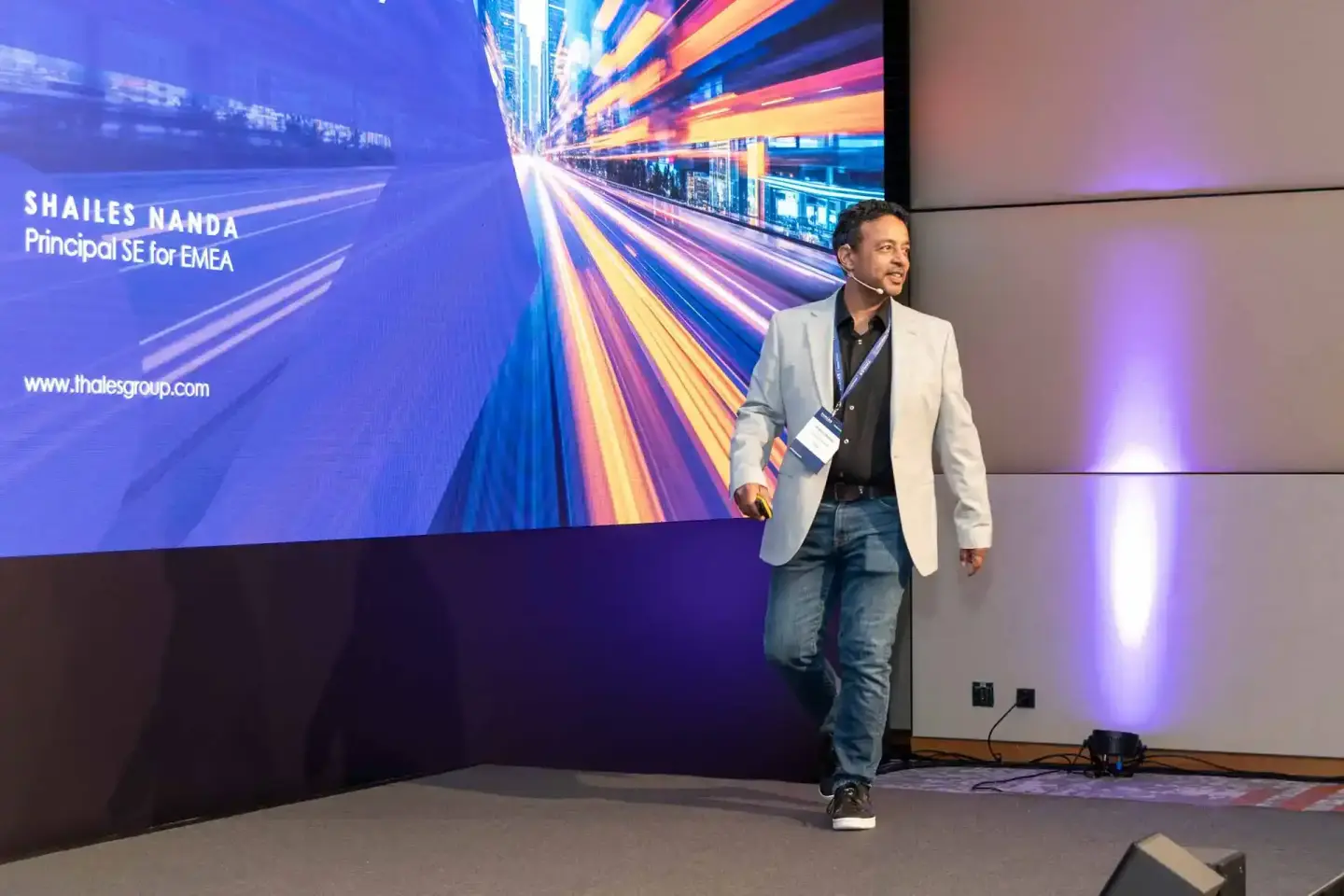 Sprecher Shailes Nanda bei Thales Firmenevent Wien präsentiert vor großem Display mit abstraktem Motion-Grafik-Hintergrund