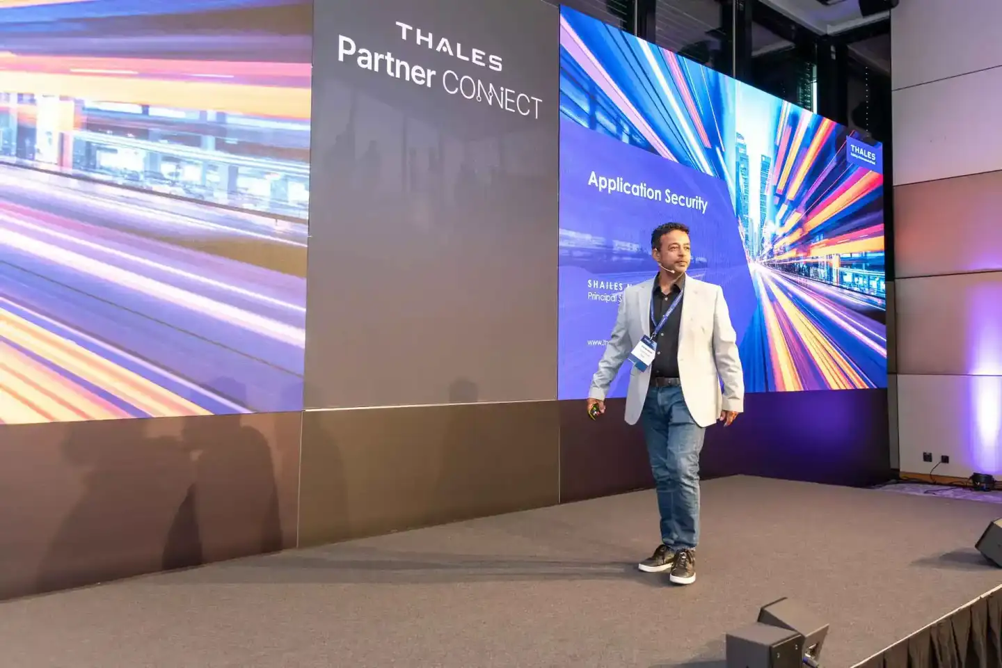 Eventfotograf präsentiert bei Thales Partner Connect Konferenz vor großem Display mit Application Security Inhalten