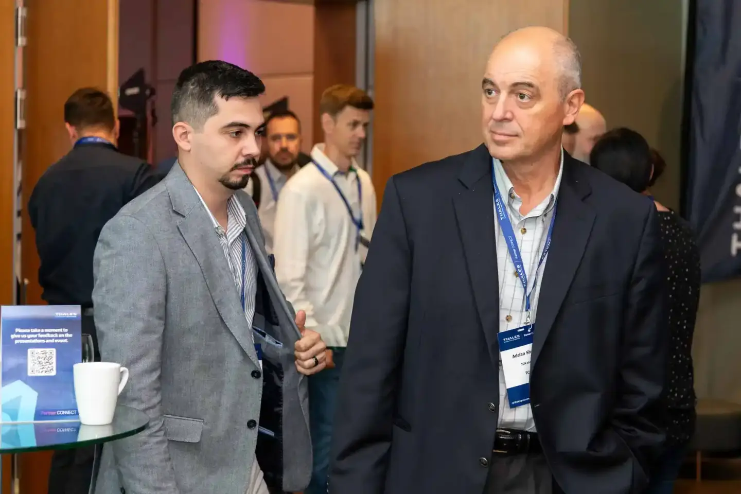 Zwei Geschäftsmänner im Gespräch auf einem Firmenevent Wien, im Hintergrund weitere Teilnehmer und Eventausstattung