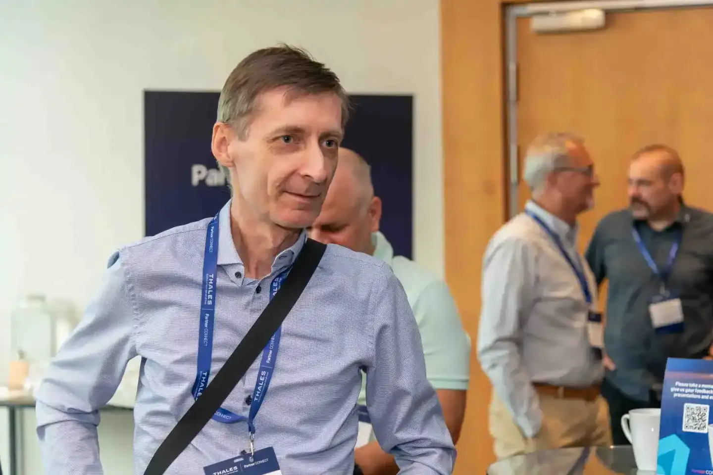 Eventfotograf dokumentiert Geschäftsmann mit Lanyard bei Thales-Firmenevent in Wien, weitere Teilnehmer im Hintergrund