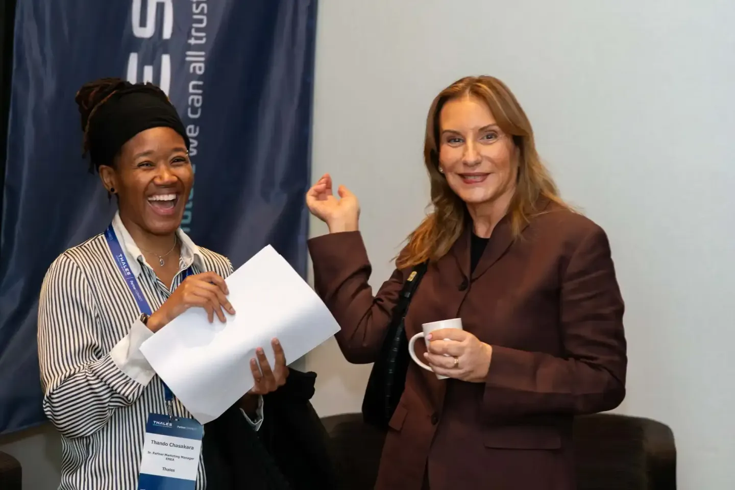 Zwei Frauen bei einem Thales Firmenevent in Wien, eine mit Lanyard und Dokumenten, beide lächelnd im Gespräch